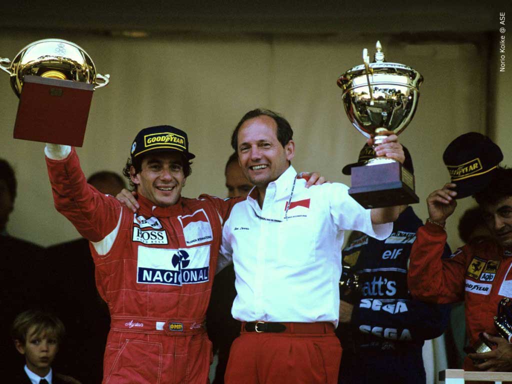 Ayrton Senna ao lado de Ron Dennis no pódio do GP de Mônaco de 1993, com os troféus da vitória do piloto e da McLaren